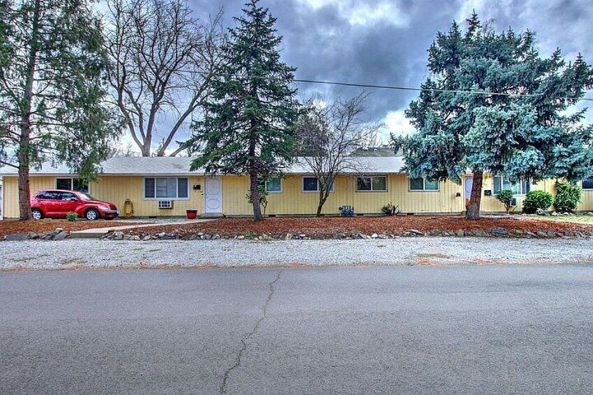 A yellow mobile home with a red car parked in front, surrounded by trees and a gravel driveway. 4