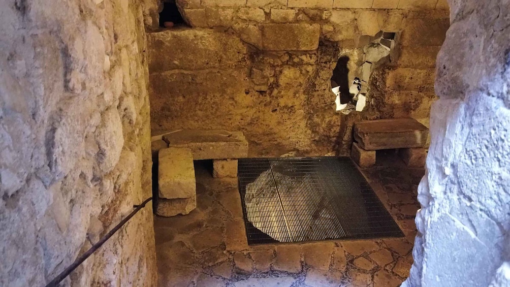 An ancient stone structure with a bench, a grid-like floor, and a wall with a small opening. 2