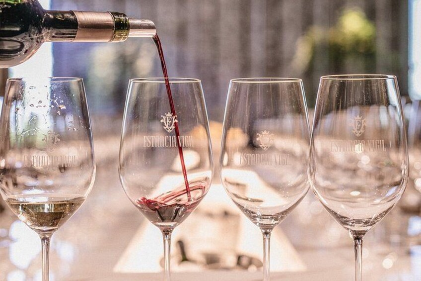 A bottle pouring red wine into a glass with a logo. 2