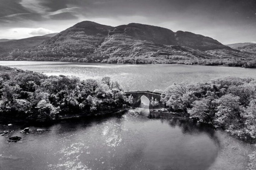 A bridge over a calm river, surrounded by hills and trees. 4