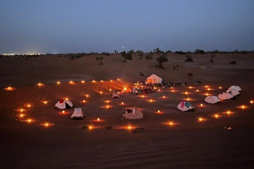 Campeggio nel deserto al crepuscolo, con tende disposte a cerchio e candele accese tutt'intorno. 1
