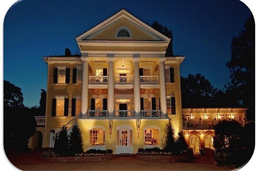 A large, illuminated mansion with a symmetrical facade, multiple balconies, and a central entrance with columns. 1