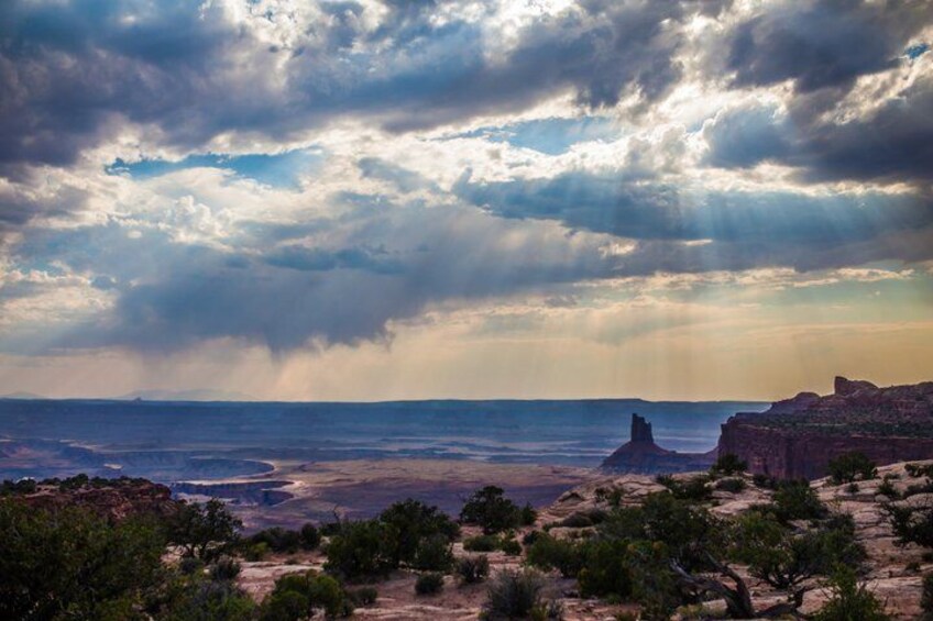 A desert landscape with a prominent rock formation, a distant mountain, and a cloudy sky. 2