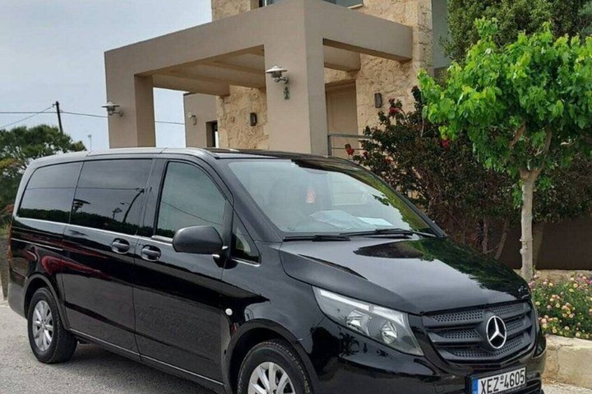 Una furgoneta negra Mercedes-Benz estacionada frente a un edificio moderno con un árbol y flores cercanas. 3