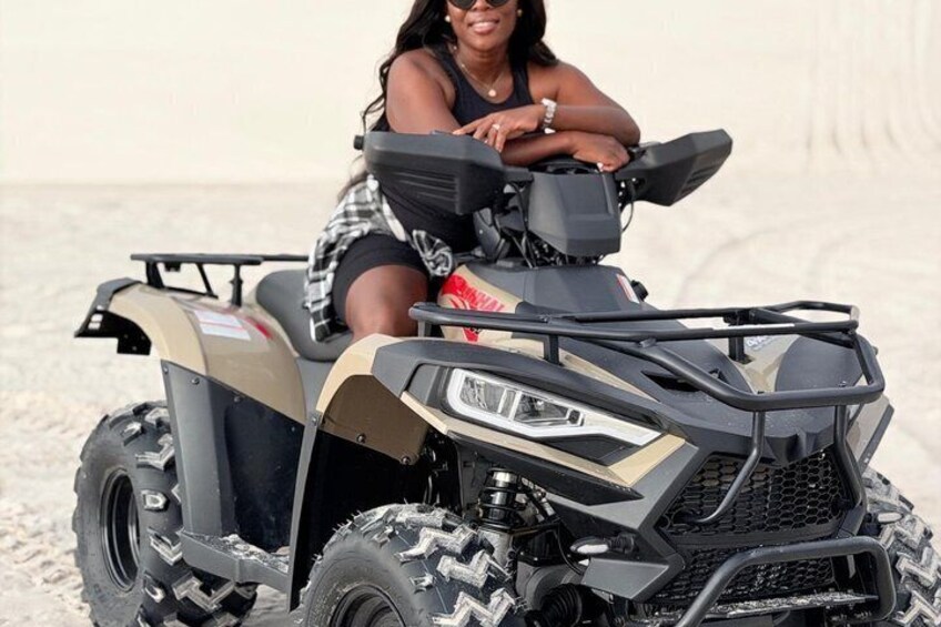 A person on a four-wheeled vehicle with a large front grille and side steps, on a sandy terrain. 3