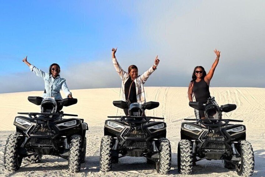 Three people on ATVs in a desert with sand dunes in the background. 4