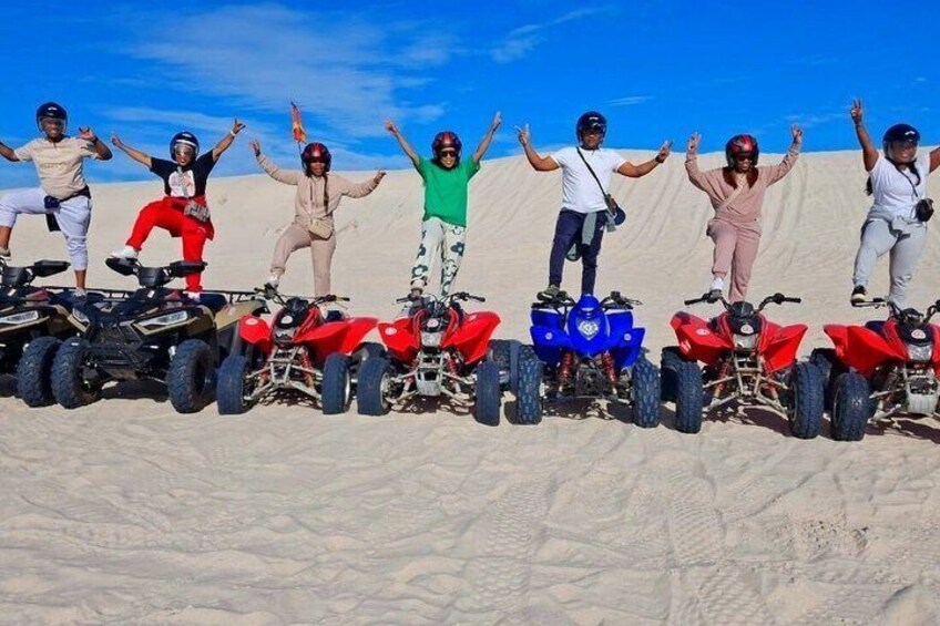 A group of people on ATVs in a desert with sand dunes in the background. 1