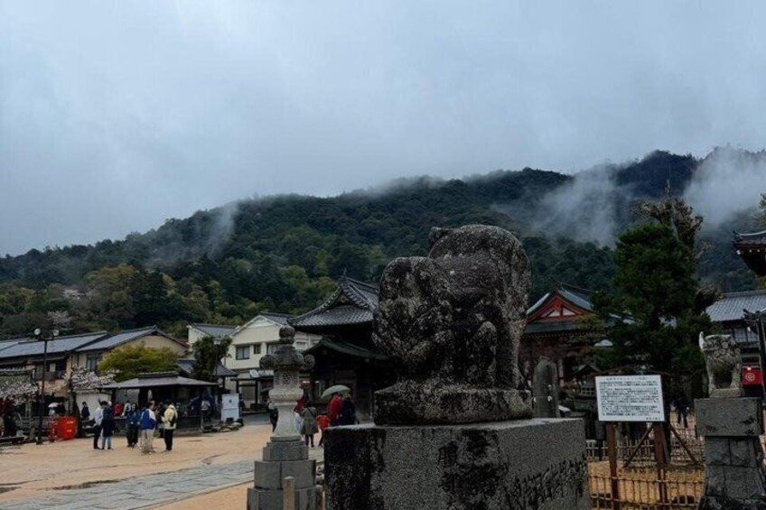A stone lion statue in a traditional Japanese setting with buildings and misty mountains in the background. 4