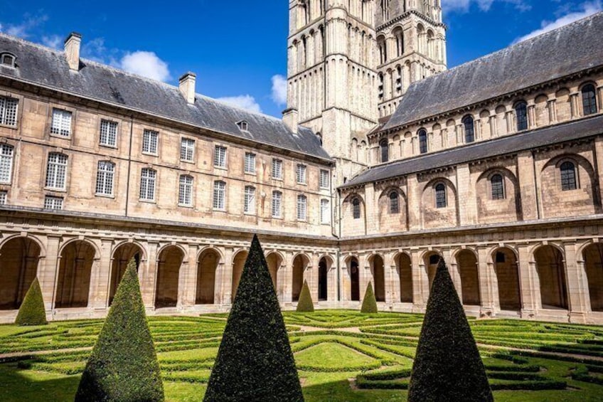 A courtyard with geometrically shaped hedges and a historic building with arched windows and a tower. 3