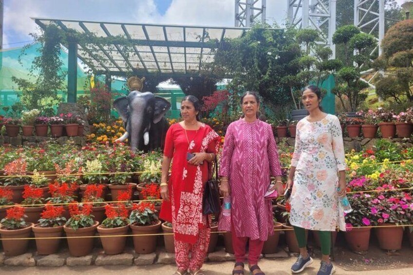 Three people standing in front of a variety of potted plants and a large elephant statue. 2