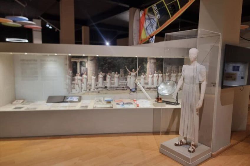 A mannequin in a white dress inside a glass display case with a background of a historical scene. 1