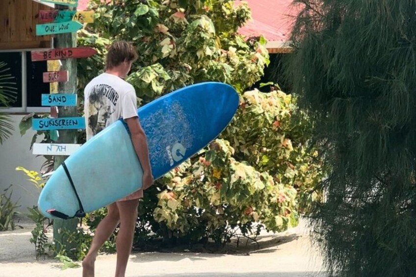A person holding a surfboard, standing next to a signpost with various signs. 1