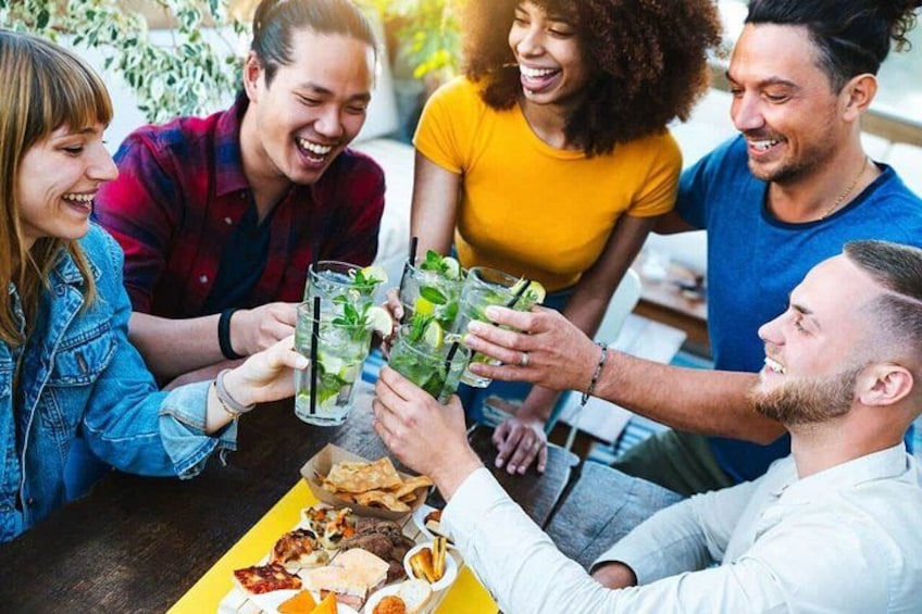 A group of people toasting with drinks at a table with food. 1