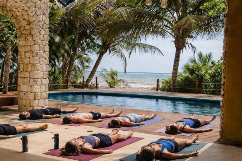 People lying on mats by a pool with a beach and palm trees in the background. 3