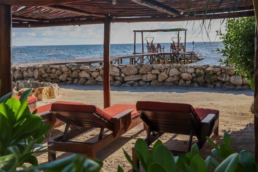 A beachside lounge with wooden chairs and a table, a stone wall, and the ocean in the background. 5