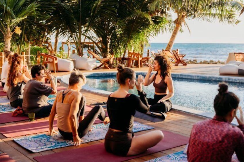 A group of people doing yoga on mats by a pool with palm trees and a view of the ocean. 1