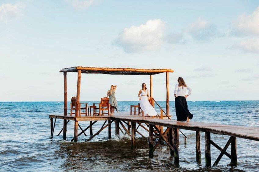 Een houten steiger die zich uitstrekt over een wateroppervlak, met een rieten dakgebouw en stoelen. 5
