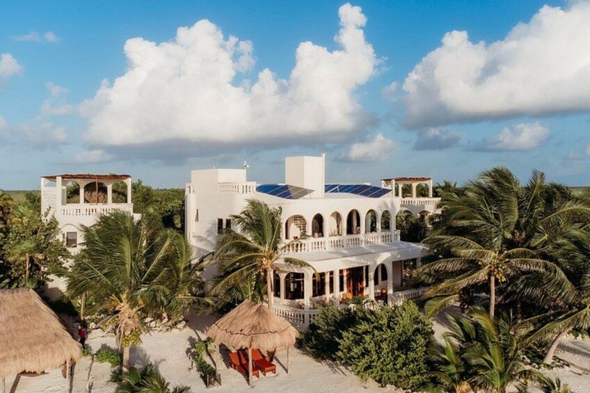 Een resort met witte gebouwen, palmbomen en hutten met rieten daken. 3
