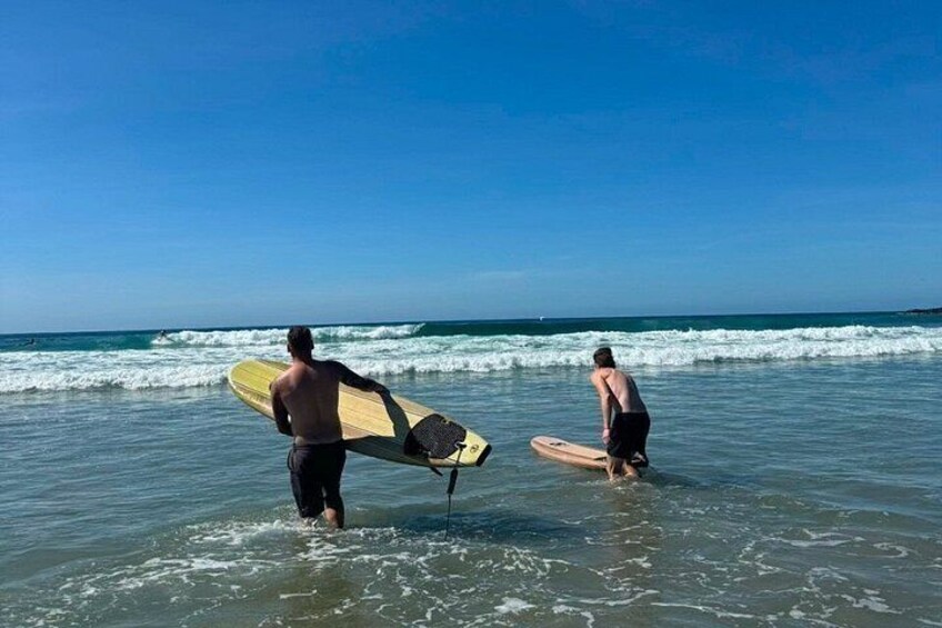 Dos personas de pie en aguas poco profundas en la playa, cada una sosteniendo una tabla de surf. 3