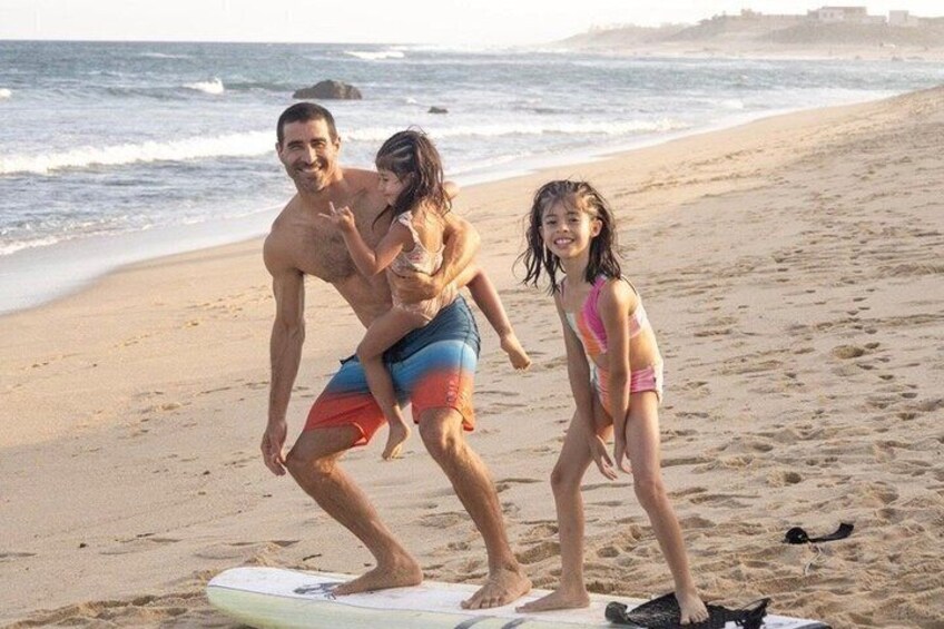 Un hombre y dos niños en una playa con una tabla de surf. 1