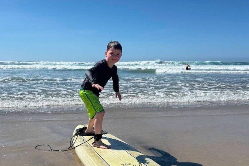 A person standing on a surfboard at the beach with waves in the background. 1