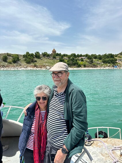 Two people on a boat with a rocky shoreline and a church in the background. 3