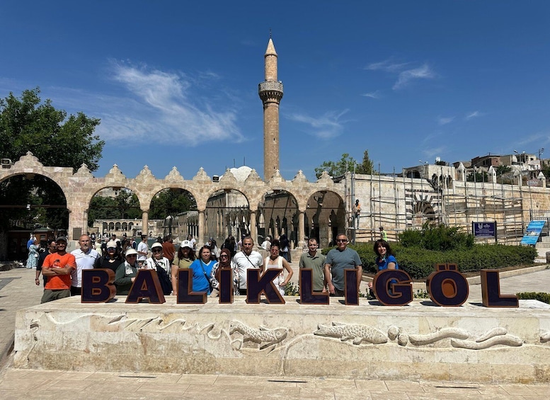 A group of people standing in front of the BULKIGÖL sign with a historic building and a minaret in the background. 2