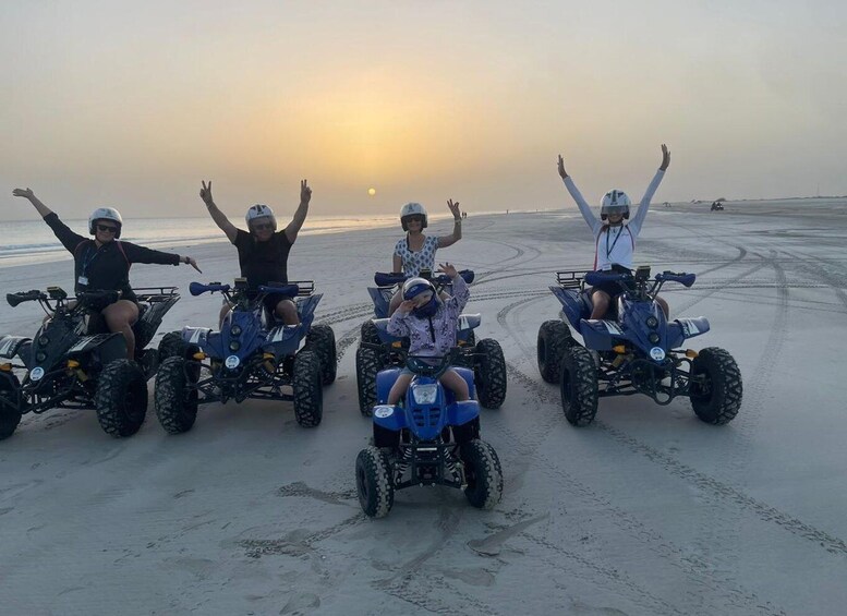 Four people on ATVs on a beach with the sun setting in the background. 2