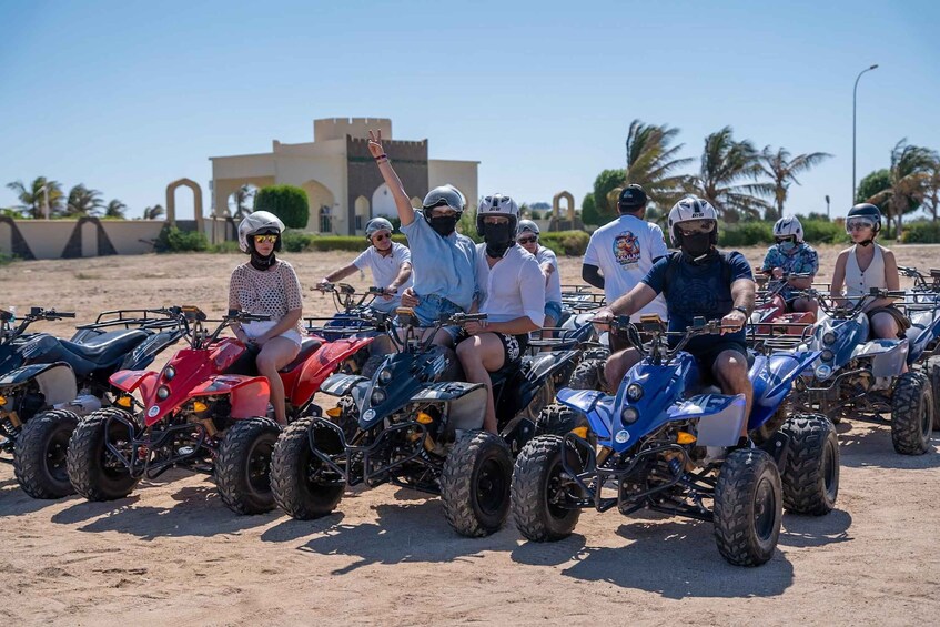 A group of people on quad bikes in a desert setting with palm trees and a building in the background. 5