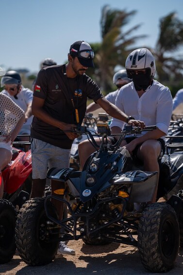 Two people on ATVs, one wearing a helmet and the other in a cap, with a crowd and palm trees in the background. 4