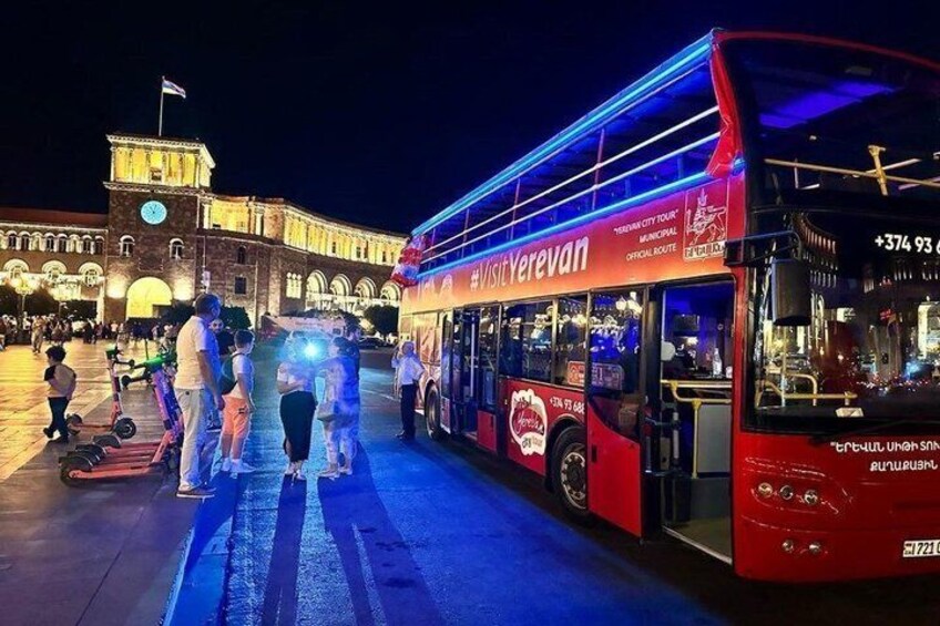 Ein roter, zweistöckiger Bus mit der Aufschrift 'Visit Yerevan', der an einer Bushaltestelle mit Personen in der Nähe geparkt ist. 3