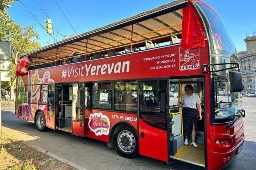 Ein roter Bus mit der Aufschrift 'Visit Yerevan' und 'Yerevan City Tour', der an einer Bushaltestelle geparkt ist. 2