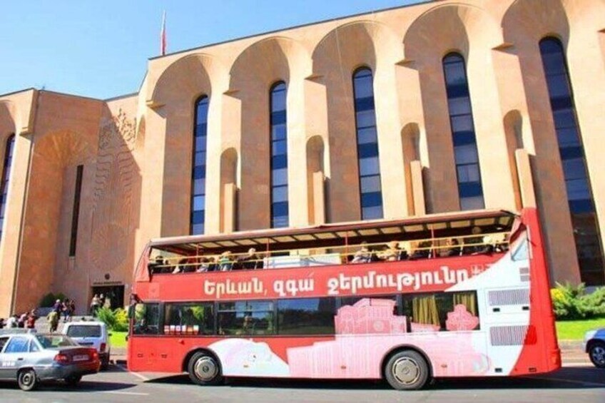 Ein roter, zweistöckiger Bus vor einem Gebäude mit Rundbogenfenstern. 4