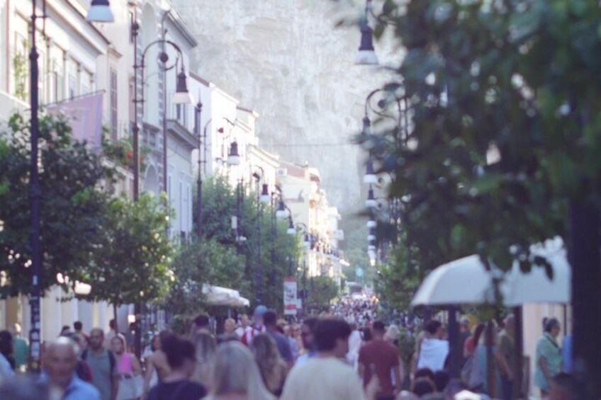 Calle concurrida flanqueada por árboles y edificios, con gente caminando y algunos parados. 3