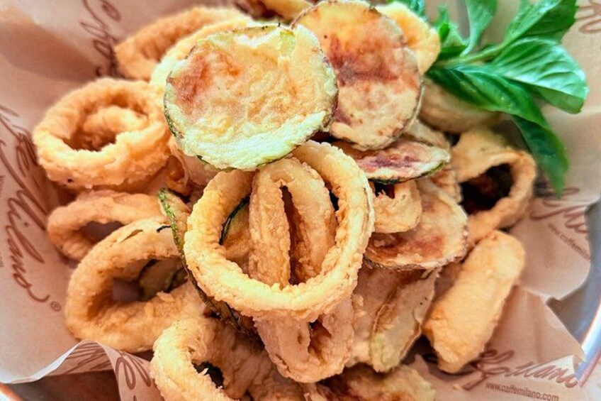 A basket of fried calamari rings with a garnish of green leaves. 2