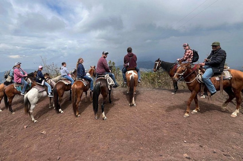 A group of people riding horses on a dirt path with a cloudy sky in the background. 1
