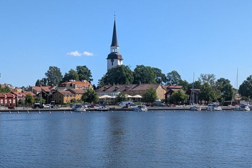 Eine Stadt am Wasser mit einem markanten Kirchturm, Booten, die an der Küste liegen, und Wohnhäusern. 2