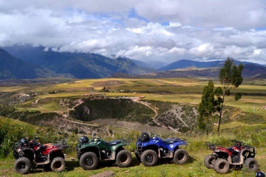 A mountainous landscape with four off-road vehicles parked on a grassy area. 5