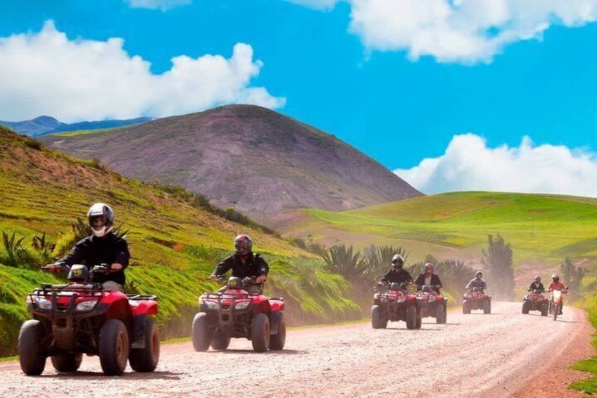 A group of riders on quad bikes on a dirt road surrounded by hills. 2