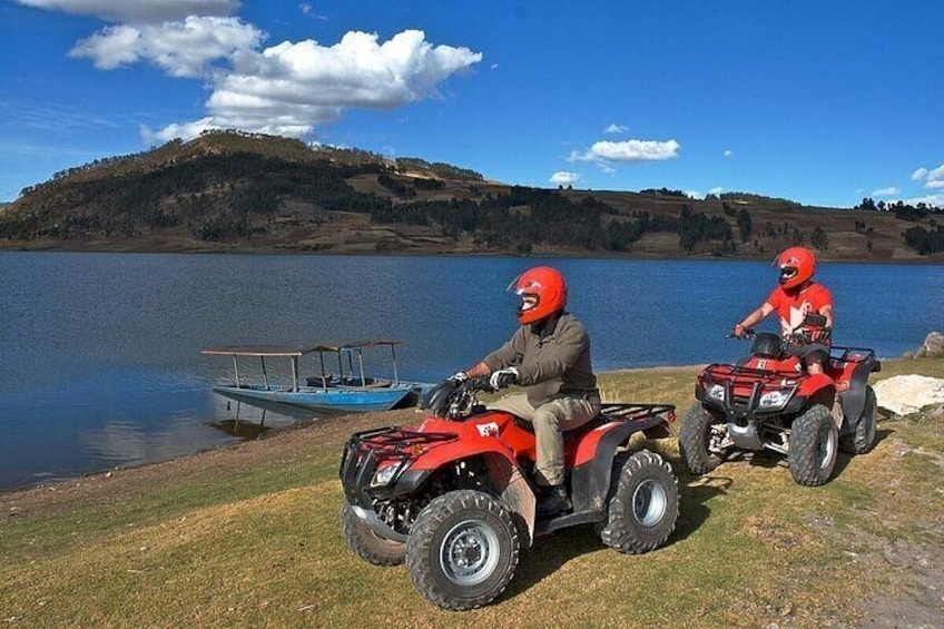 Two people on red ATVs by a lake with a dock and hills in the background. 1