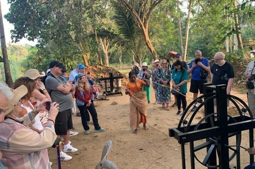 A group of people gathered around a traditional black water wheel in a forested area. 1