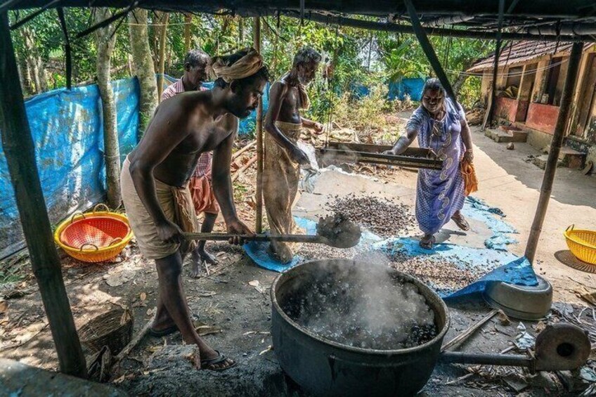 People processing coffee beans in an outdoor setting with a large pot and a blue tarp. 5