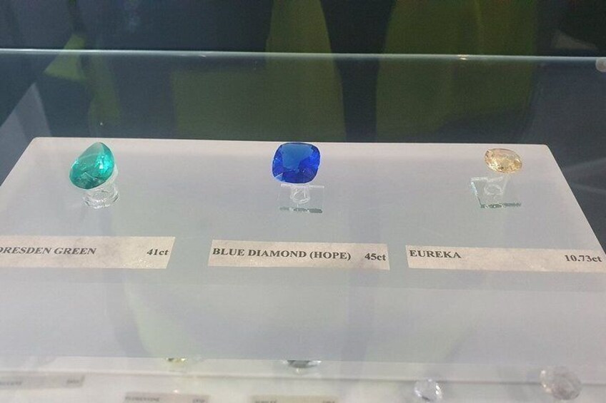Trois pierres précieuses : le diamant vert de Dresde, le diamant bleu (Hope) et l’Eureka, chacune étant accompagnée d’une étiquette descriptive et présentée dans une vitrine. 1