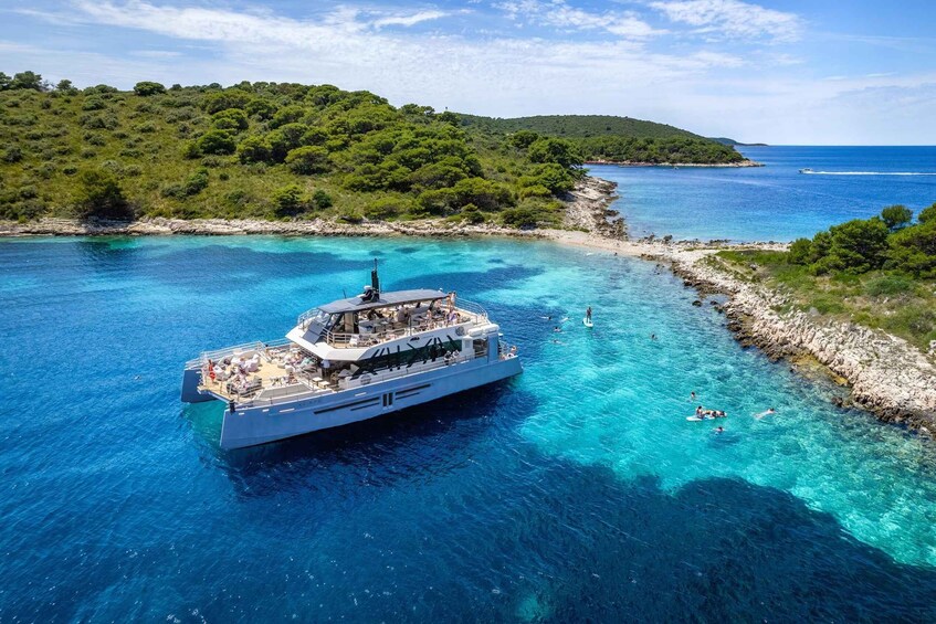 A large boat with people on deck, surrounded by clear blue water and a rocky coastline with greenery. 1