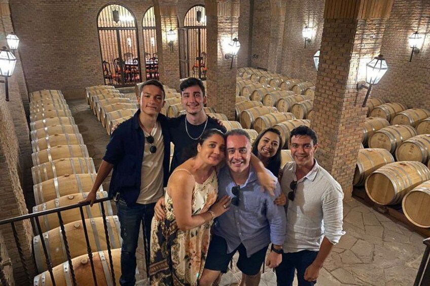 A group of people in a wine cellar with rows of wooden barrels and brick walls. 5