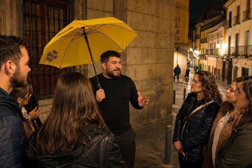 A group of people standing on a city street at night, one person holding a yellow umbrella. 3
