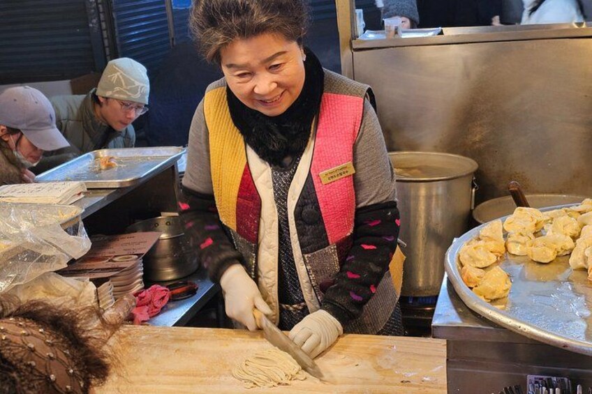 Una persona preparando comida en una barra con tabla de cortar, una olla y una bandeja de alimentos. 4