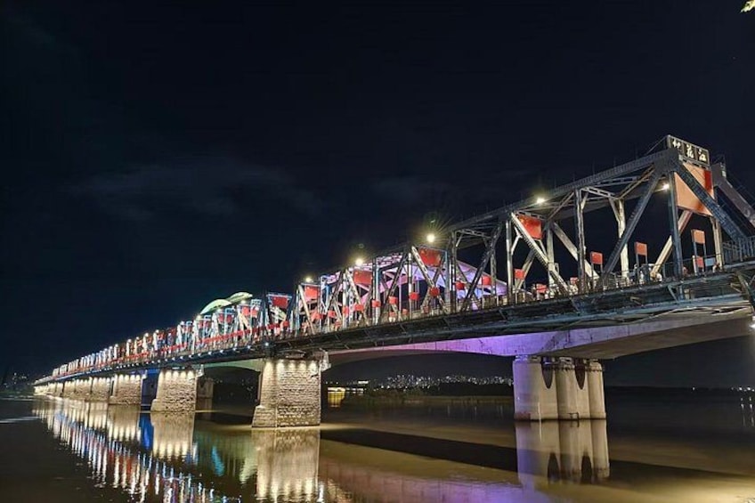A brightly lit bridge at night with colorful lights reflecting on the water below. 5