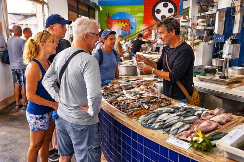 Un marché aux poissons où l’on peut voir des clients faire leurs achats et une grande variété de poissons exposés sur le comptoir. 2