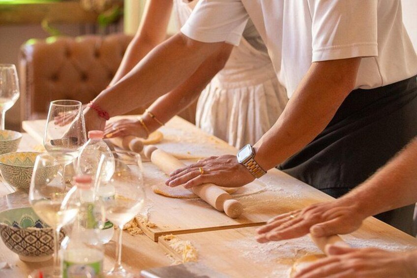 Mensen bereiden deeg op een houten tafel, met deegrollers, kommen en glazen wijn. 5